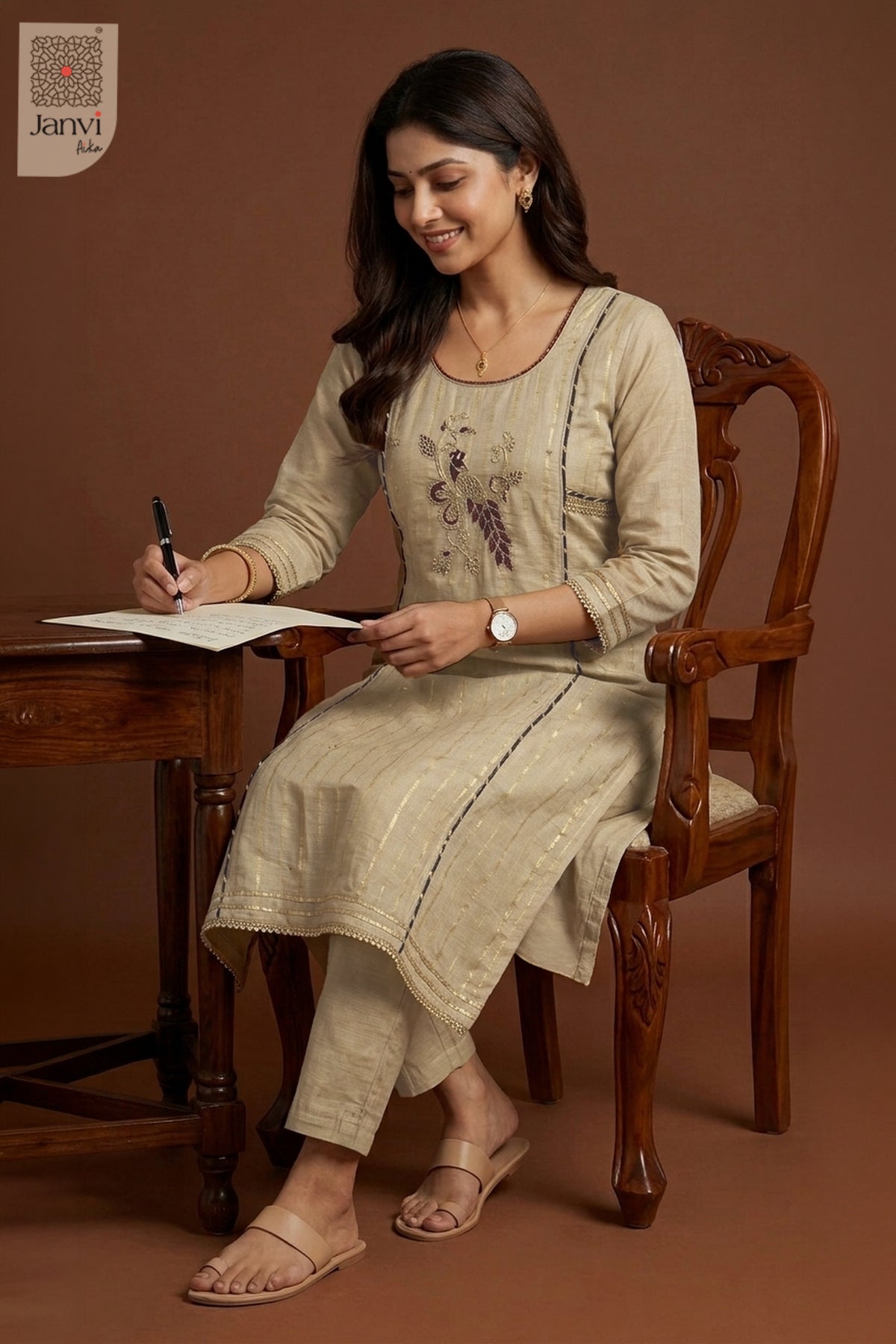 Seated lifestyle pose writing at wooden desk in a muted grayish orange chudidar set.