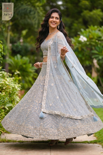 Standing side profile shot of a beautiful ice blue net lehenga price to complete the festive look.