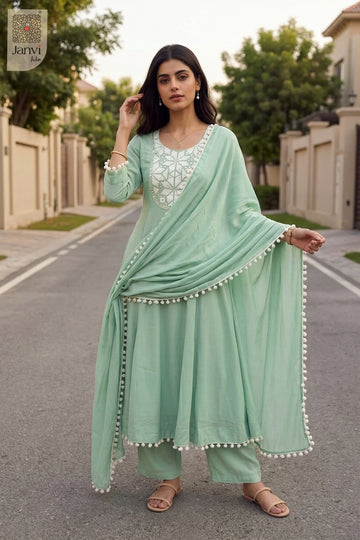 Outdoor pose displaying pom pom tassel borders on a soft cyan churidar set with dupatta.