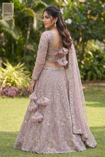 This rear full standing shot showcases a gorgeous rose gold/dusty lilac net lehenga set.