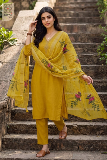 Standing on outdoor stone stairs holding printed scarf in a party wear churidar set.