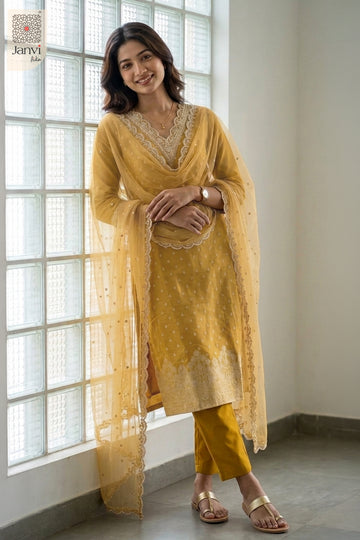 Poised portrait by a grid window wearing an ornate dijon yellow silk churidar set.