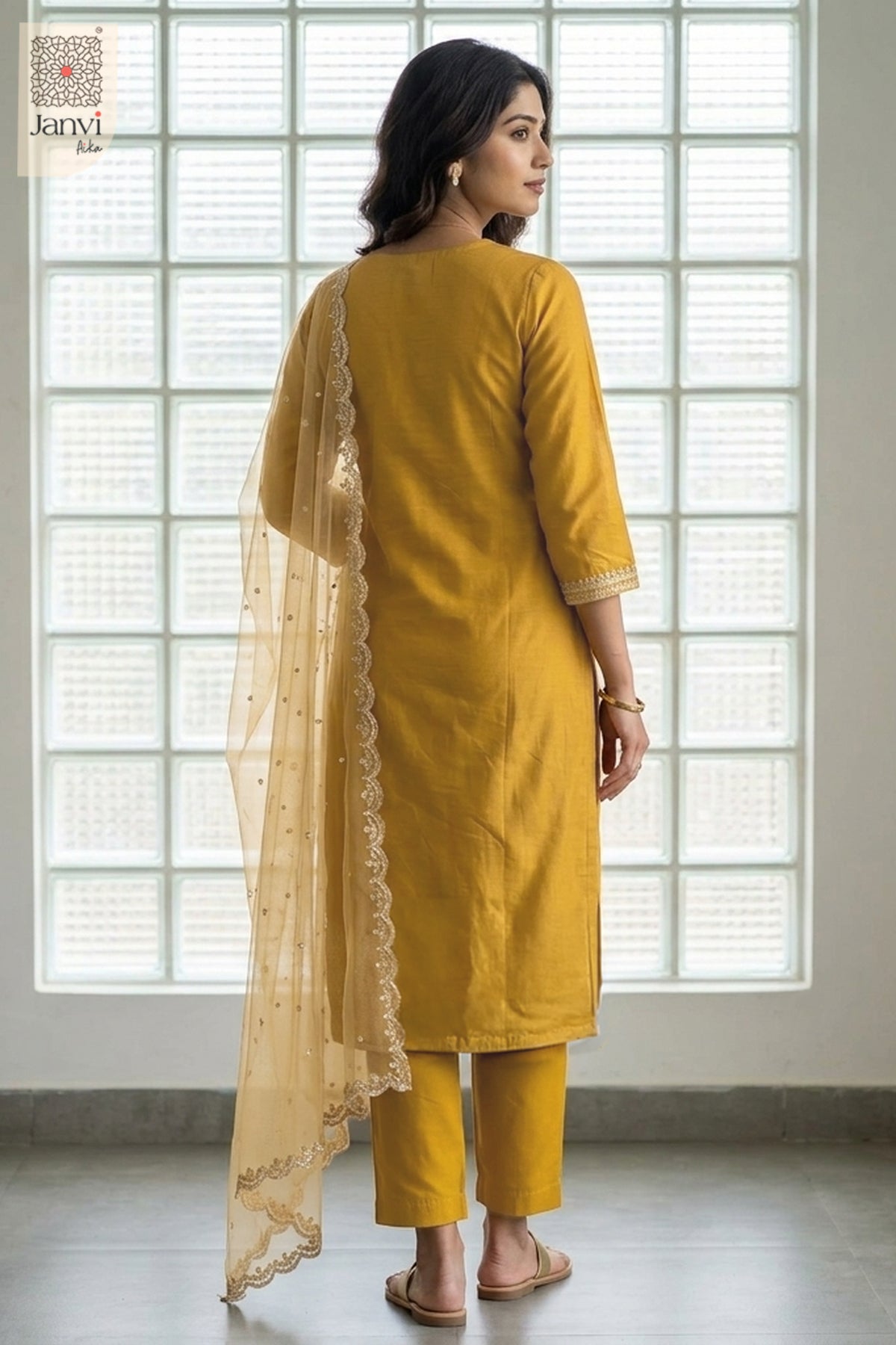 Rear view by a gridded window in a tailored dijon yellow churidar sleeves kurti suit.