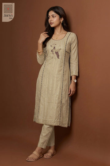 Side profile standing pose leaning on wall wearing grayish orange silk churidar set.