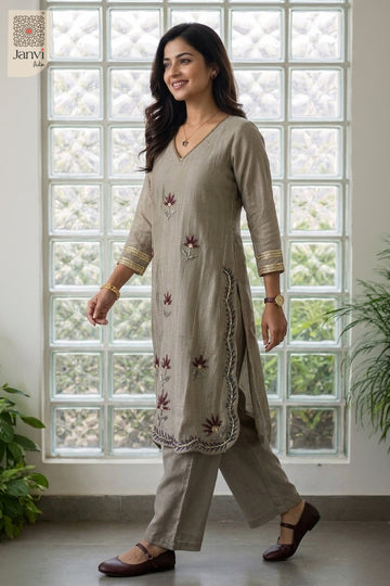 Front standing view smiling by glass blocks in a grayish blue silk churidar set.