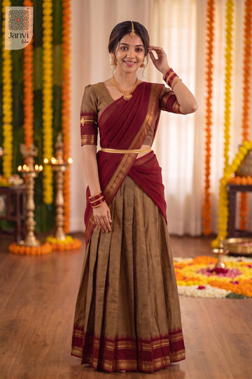 Standing pose touching hair in a festive bronze and maroon half saree lehenga attire.