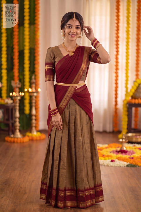 Standing pose touching hair in a festive bronze and maroon half saree lehenga attire.